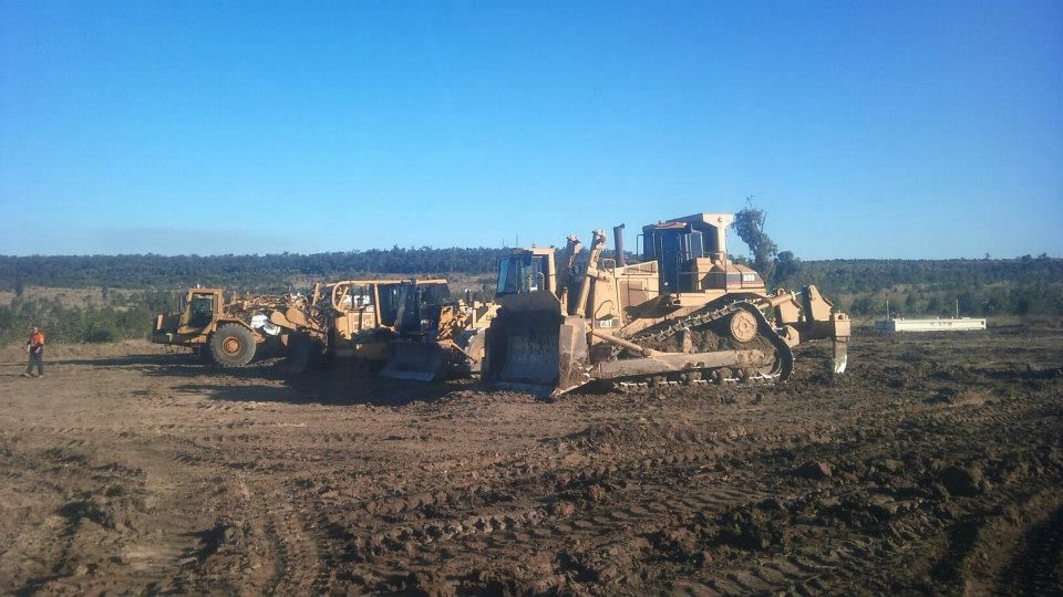 Heavy Machinery Working on a Muddy Construction Site Under a Clear Blue Sky — Oakleigh Earthmoving in Chinchilla, QLD