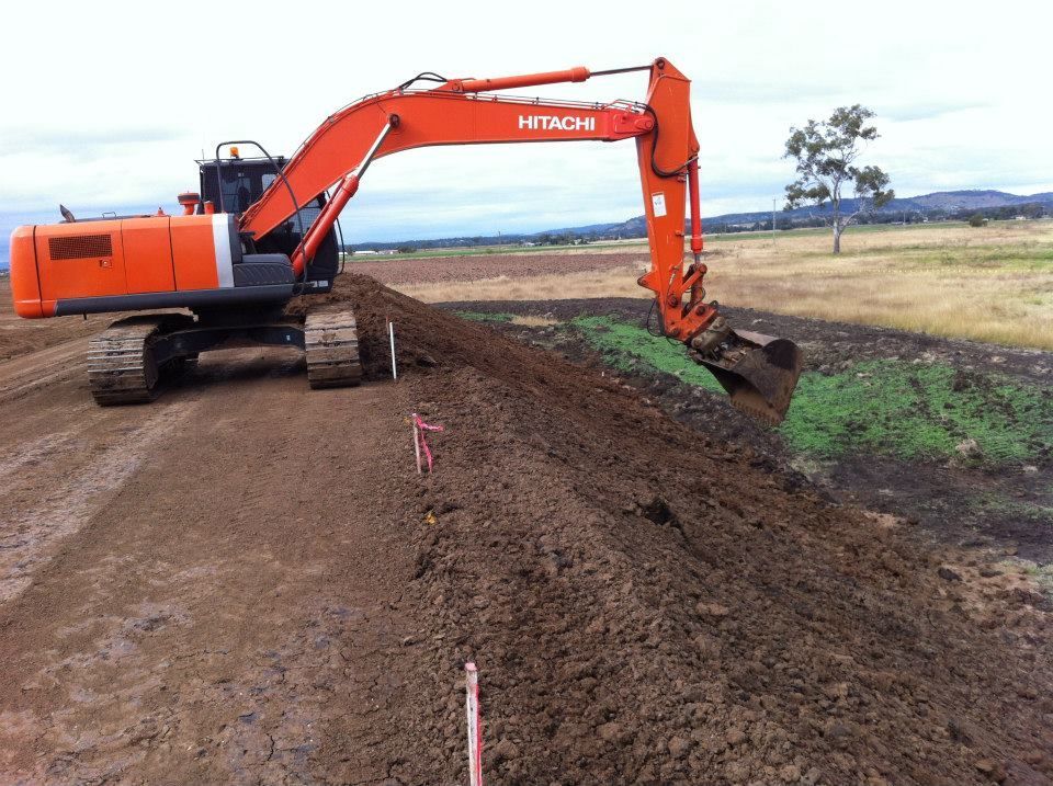 Orange Excavator Digging a Trench Beside a Dirt Road in a Rural Field — Oakleigh Earthmoving in St George, QLD