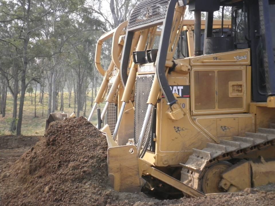 Yellow Bulldozer Pushing a Dirt Pile in a Wooded Area — Oakleigh Earthmoving in Chinchilla, QLD