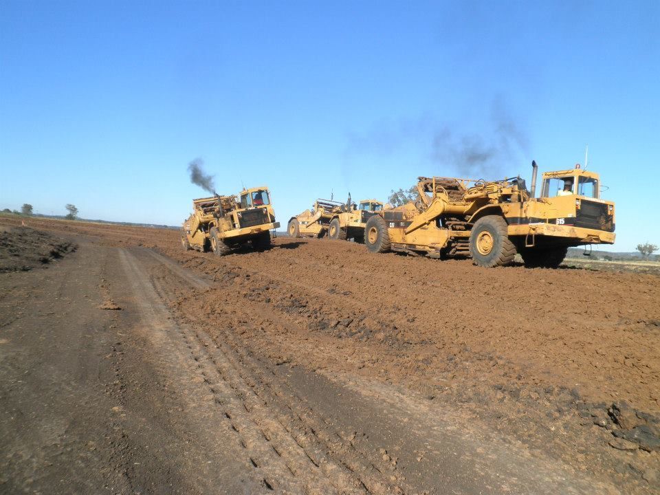 Heavy Construction Machinery Grading a Dirt Road Under a Clear Blue Sky — Oakleigh Earthmoving in Chinchilla, QLD