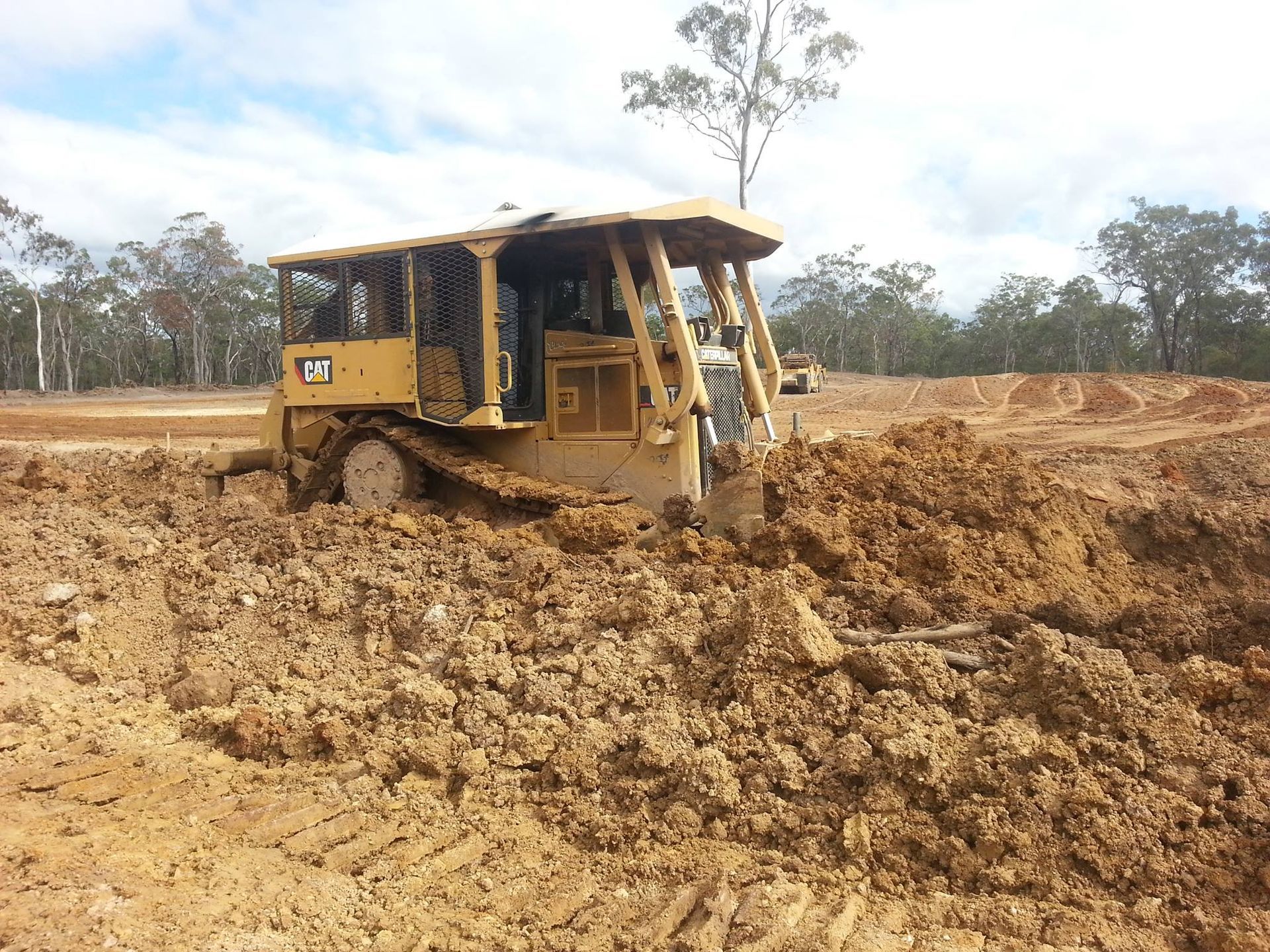 Yellow Bulldozer Pushing Mud in a Muddy Construction Site Under a Cloudy Sky — Oakleigh Earthmoving in Toowoomba, QLD