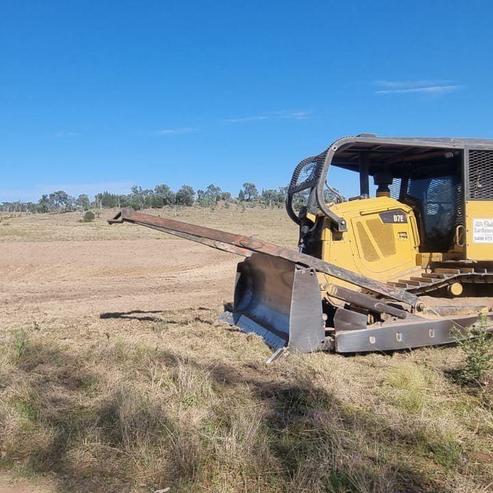 Yellow Bulldozer Pushing Dirt in a Dry Field Under a Blue Sky — Oakleigh Earthmoving in Toowoomba, QLD