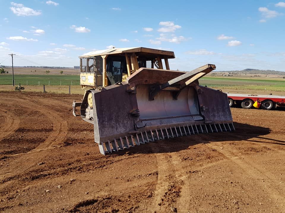 Bulldozer Leveling a Dirt Field Under a Blue Sky, With a Red Trailer in Background — Oakleigh Earthmoving in Chinchilla, QLD