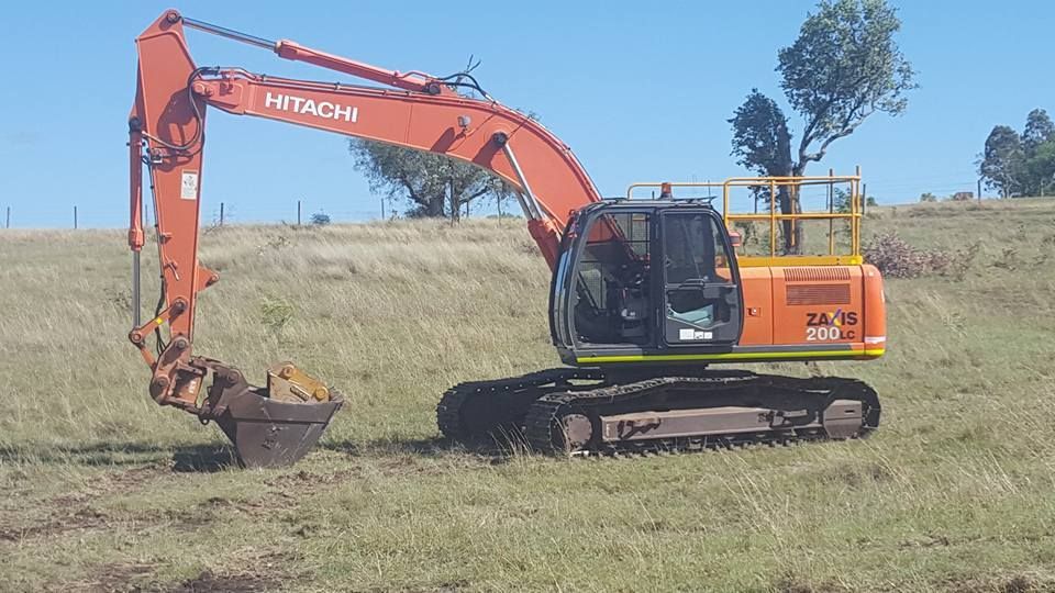 Orange Hitachi Excavator Scooping Dirt in a Grassy Field Under a Clear Blue Sky — Oakleigh Earthmoving in Toowoomba, QLD
