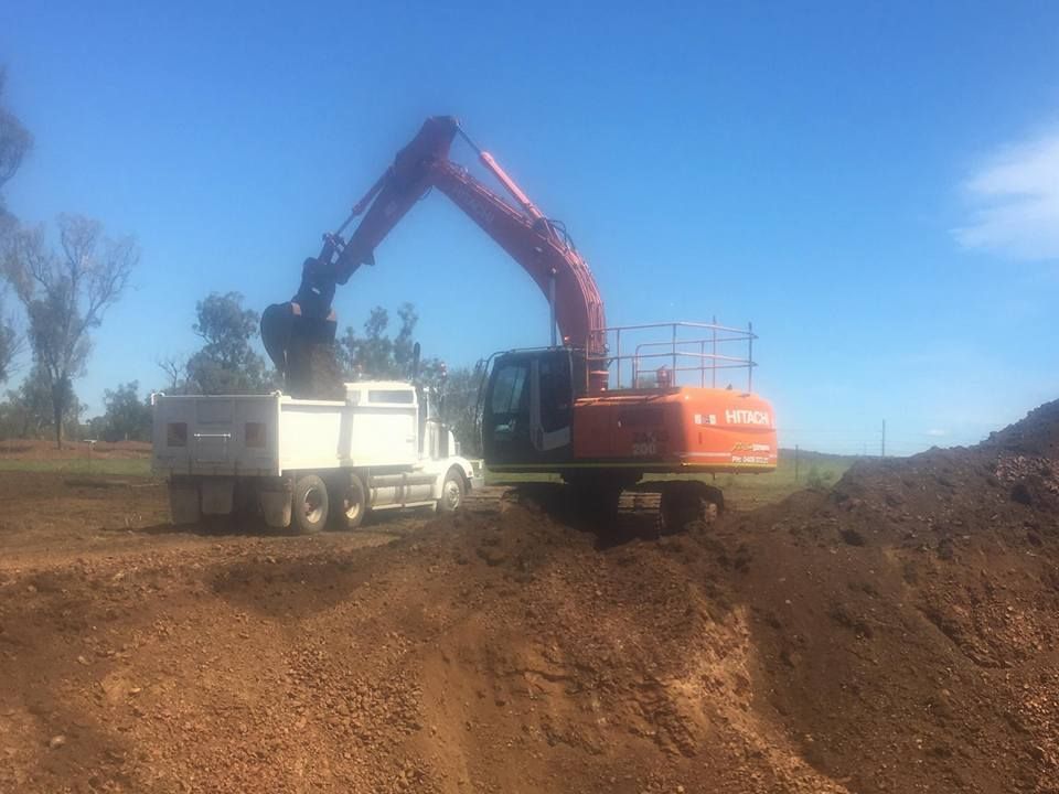 Orange Excavator Loading Dirt Into a White Dump Truck at a Construction Site — Oakleigh Earthmoving in St George, QLD