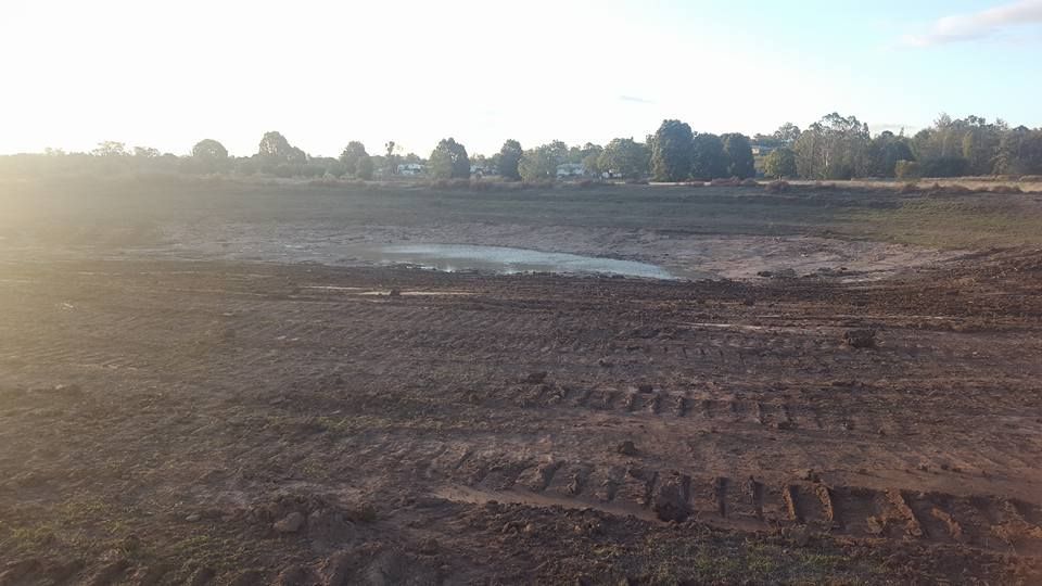 Muddy Field Under Bright Sky With Tire Tracks and a LINE of Trees in the Distance — Oakleigh Earthmoving in Chinchilla, QLD