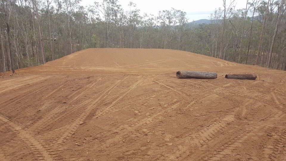 Freshly Graded Dirt Clearing in a Wooded Area With Two Logs on the Right Side — Oakleigh Earthmoving in Toowoomba, QLD