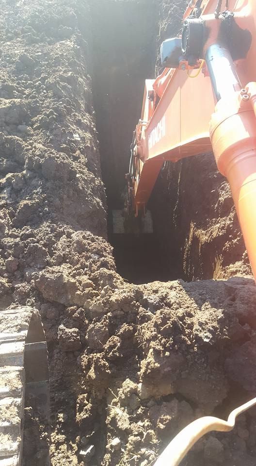 Orange Excavator Digging a Trench Beside a Dirt Wall in a Muddy Construction Site — Oakleigh Earthmoving in Kingaroy, QLD