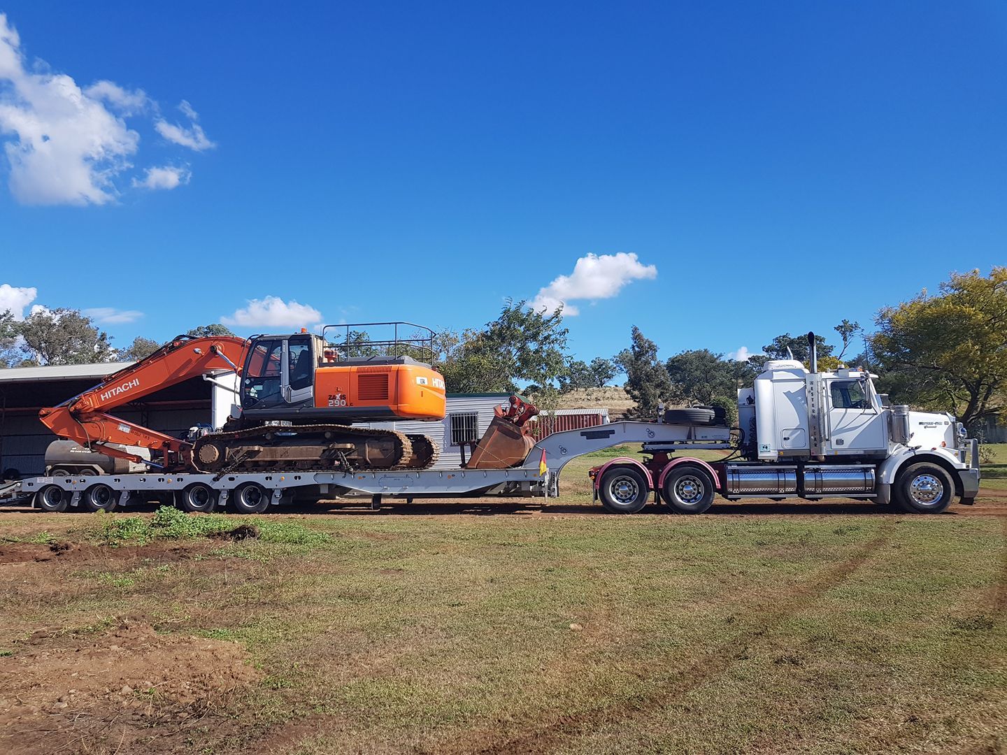White Semi Truck Hauling an Orange Excavator on a Lowboy Trailer — Oakleigh Earthmoving in Cotswold Hills, QLD