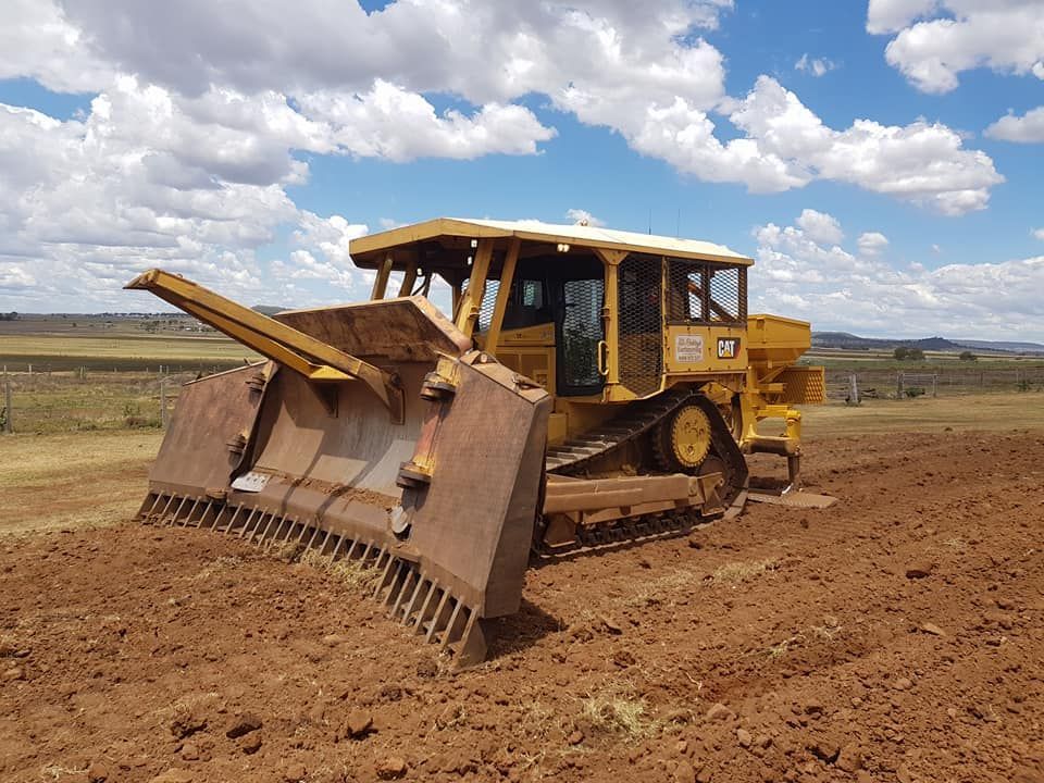 Yellow Bulldozer With Front Blade on a Dirt Road Under a Cloudy Sky — Oakleigh Earthmoving in Warwick, QLD