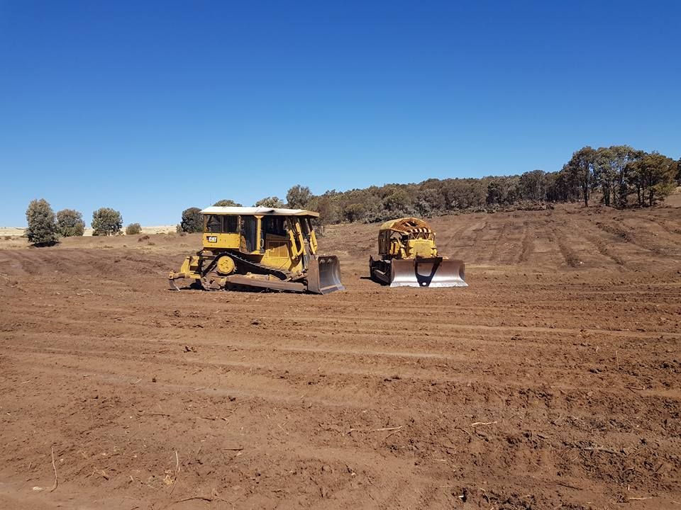 Yellow Construction Vehicles Working on a Dusty Dirt Field Under a Clear Blue Sky — Oakleigh Earthmoving in Chinchilla, QLD