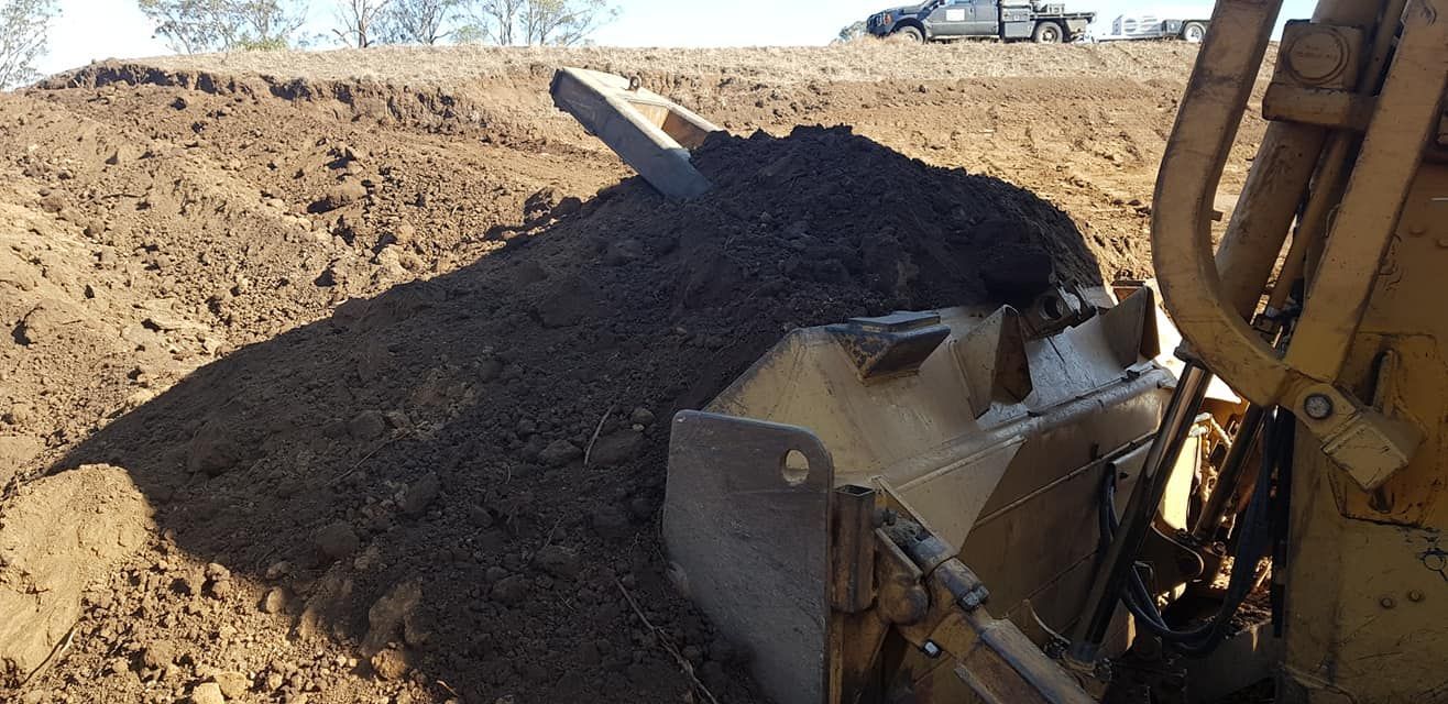 Excavator Scoops Dark Soil in a Dusty Construction Site Under Bright Sky — Oakleigh Earthmoving in Kingaroy, QLD