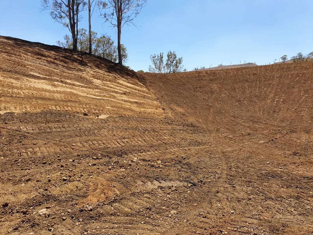 Barren Dirt Embankment Under a Clear Blue Sky, With Sparse Trees Along the Ridge — Oakleigh Earthmoving in Chinchilla, QLD