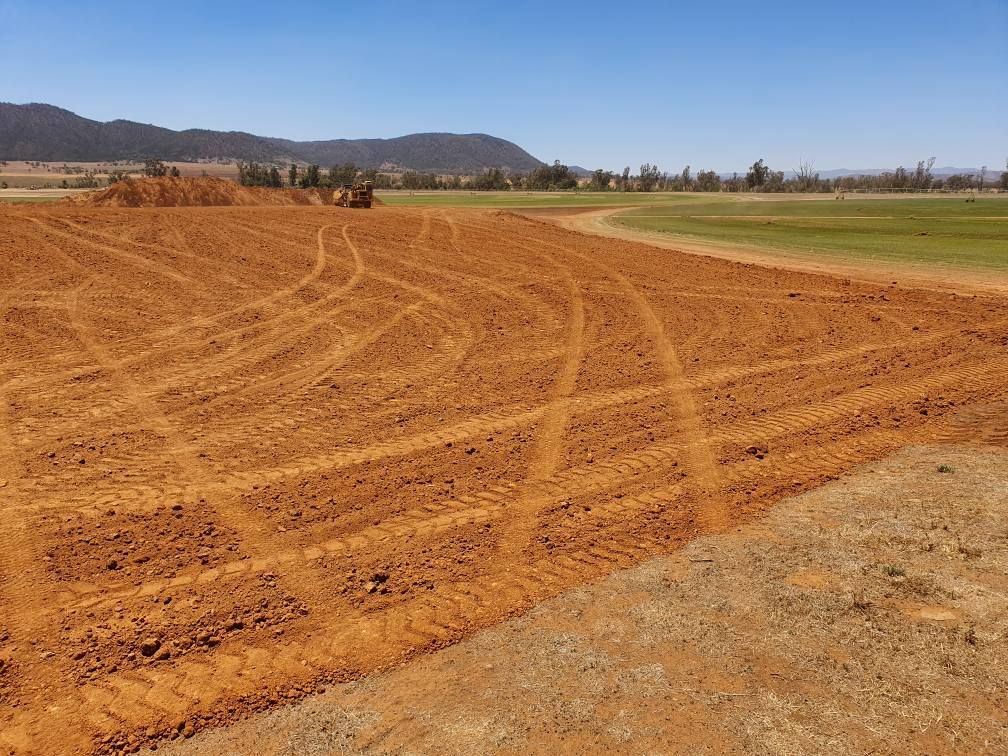 Freshly Graded Orange Dirt Field With Tire Tracks Beside a Green Sports Field — Oakleigh Earthmoving in Kingaroy, QLD