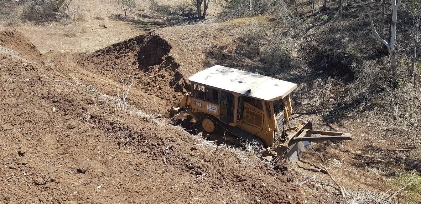 Yellow Bulldozer on a Rocky Hillside, Clearing Dirt Near a Steep Embankment — Oakleigh Earthmoving in Warwick, QLD