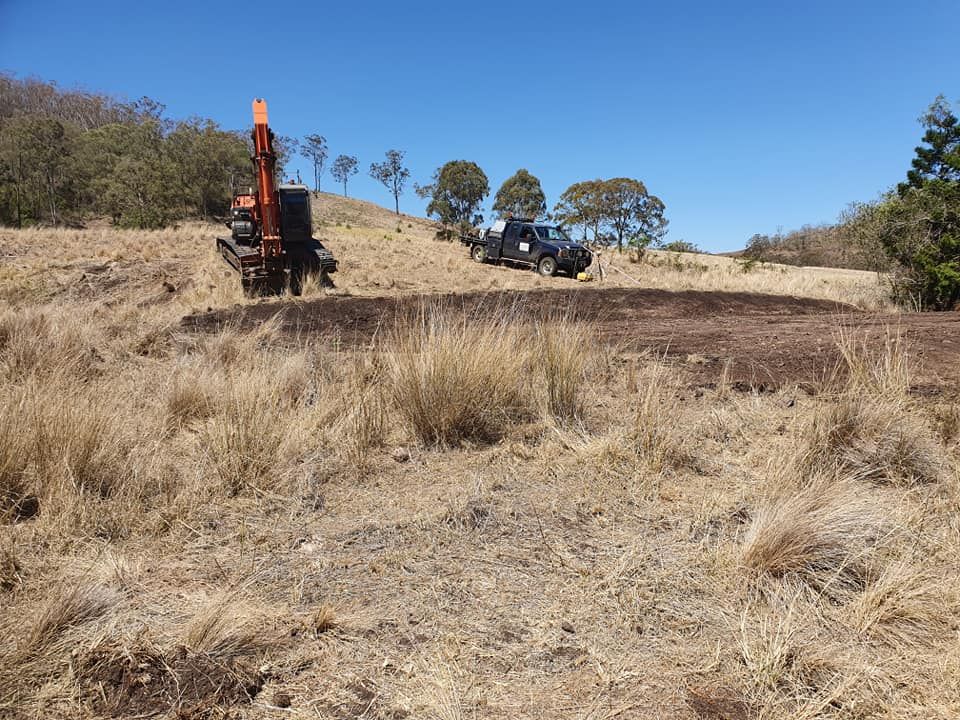 Orange Excavator and Black Truck on a Dry Dirt Hillside Under a Clear Blue Sky — Oakleigh Earthmoving in Moonie, QLD