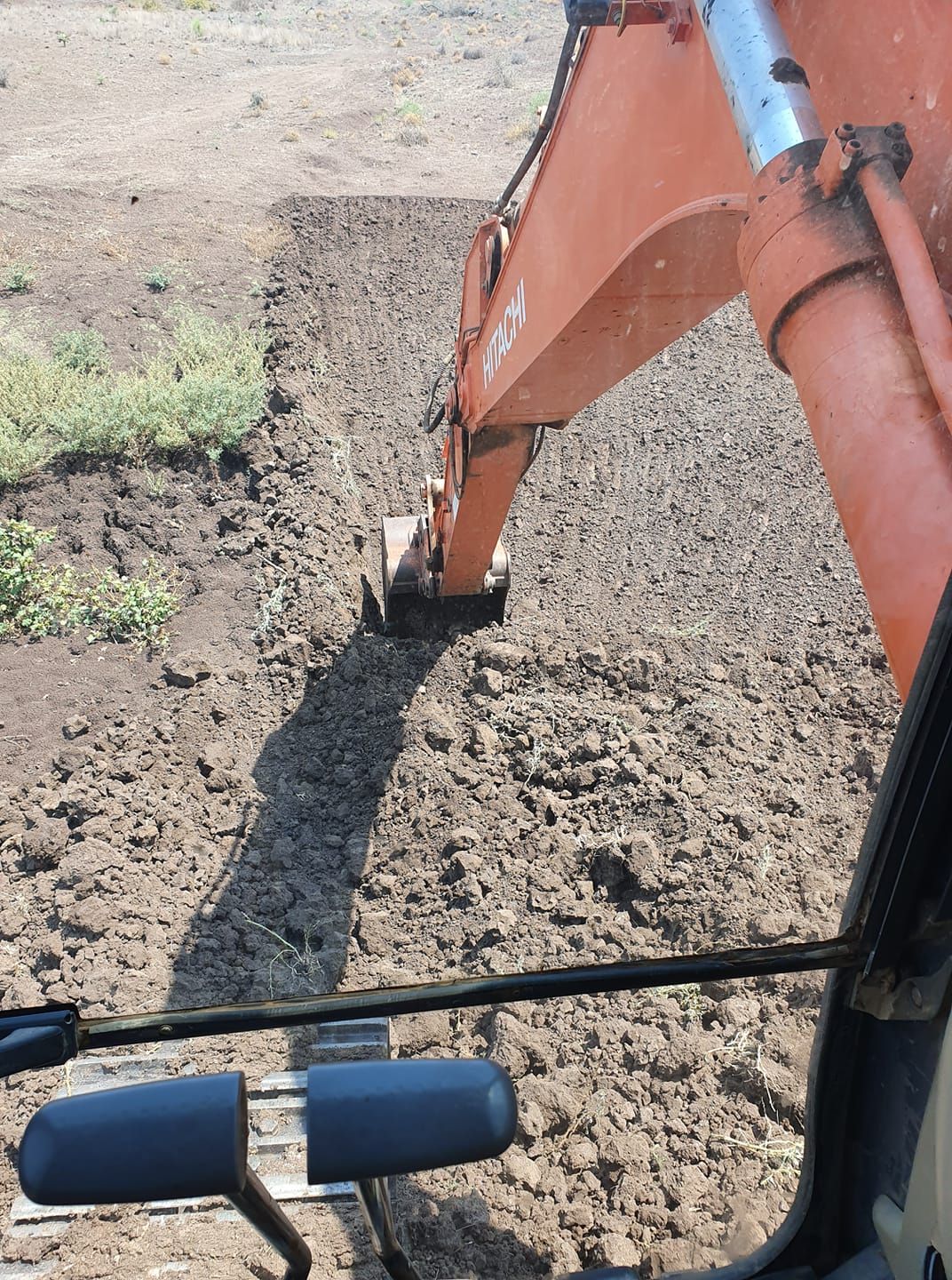 Orange Excavator ARM Digging Dirt Beside a Gravel and Grass Roadside — Oakleigh Earthmoving in Warwick, QLD