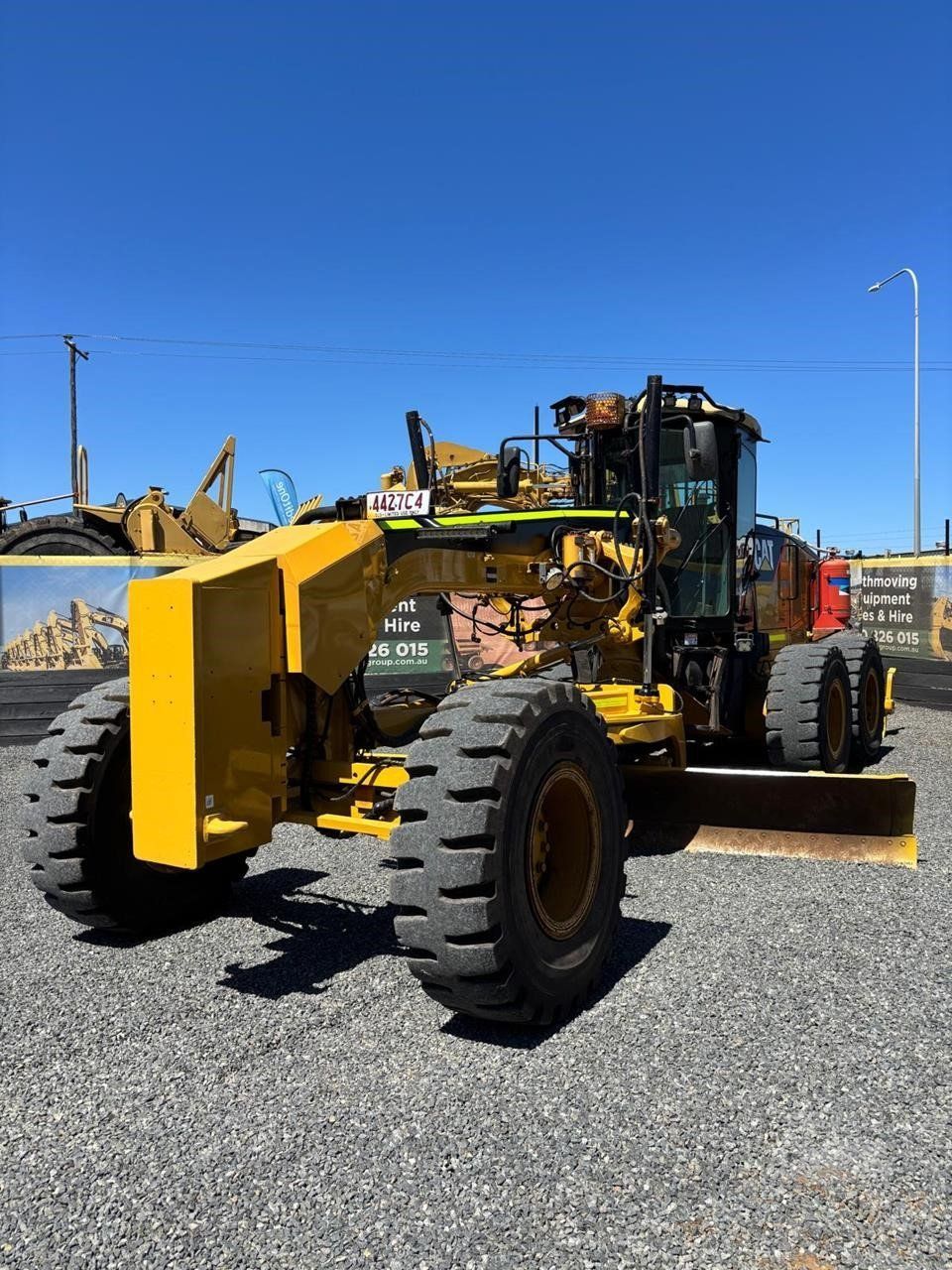 Yellow Road Grader on Gravel Lot Under Clear Blue Sky — Oakleigh Earthmoving in Cotswold Hills, QLD