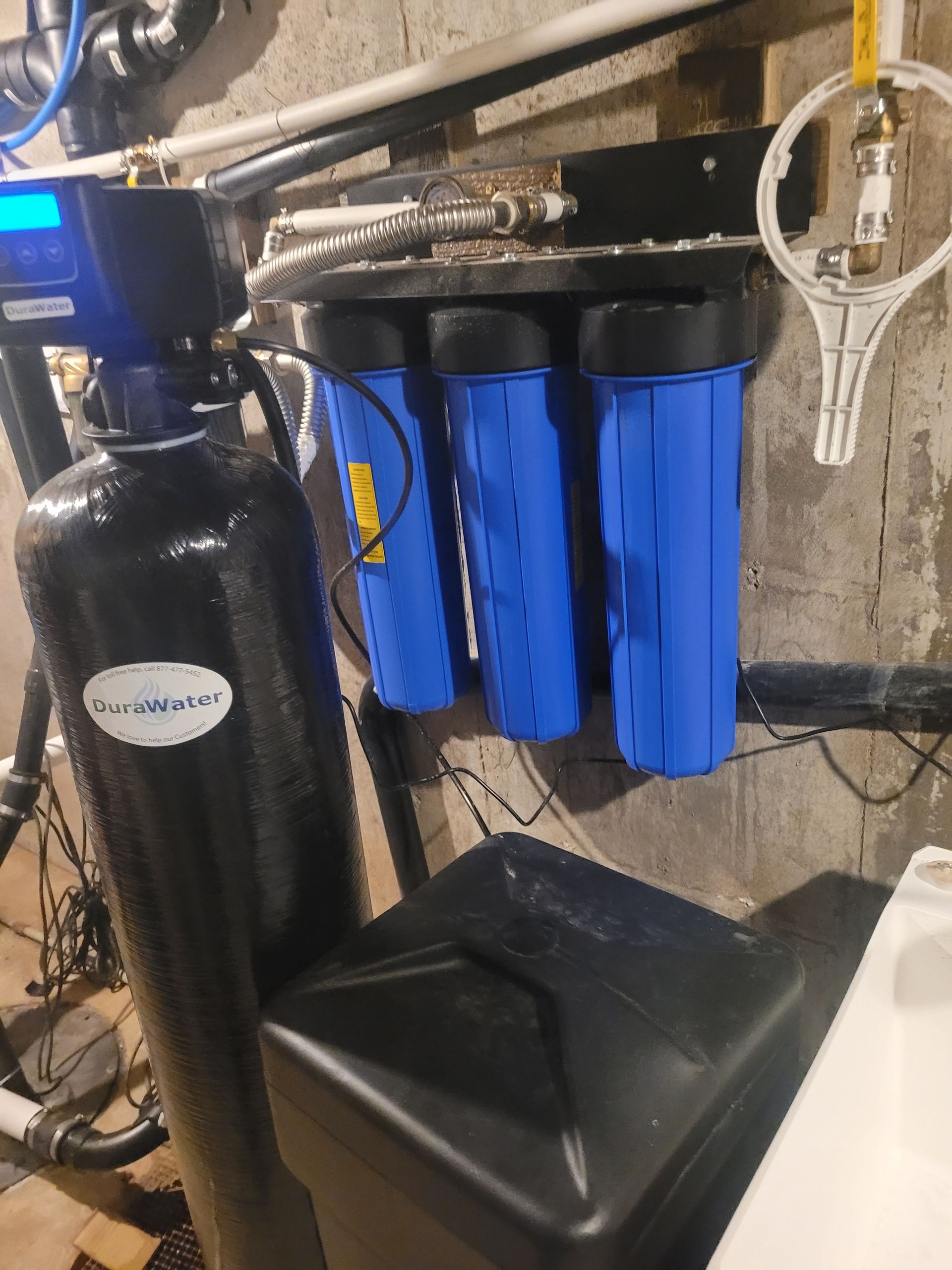 Water filtration system with four vertical beige tanks, blue piping, and a blue water storage tank in the background.