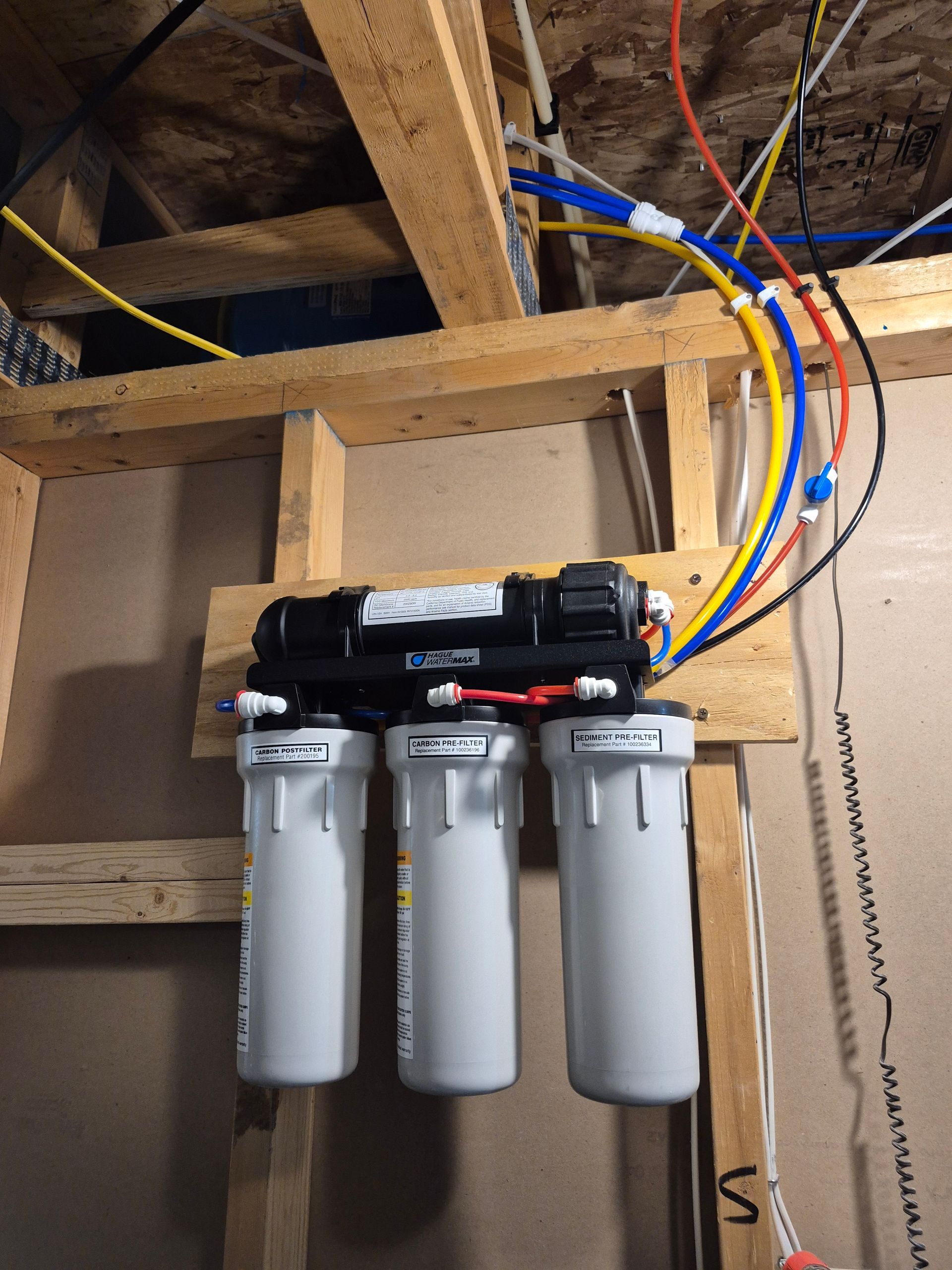Under-sink water filter and tank, plumbing visible. Blue tank left, filter right. White and grey cabinet.