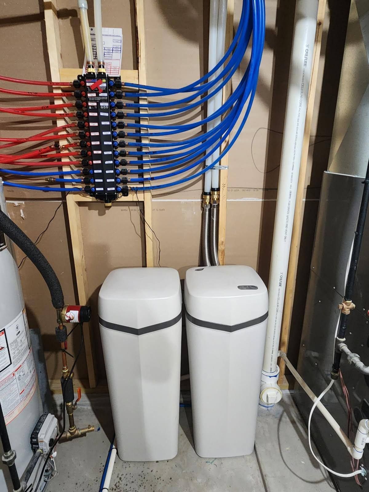 Two water softeners with blue/red pipes, a water heater, and a PEX manifold.