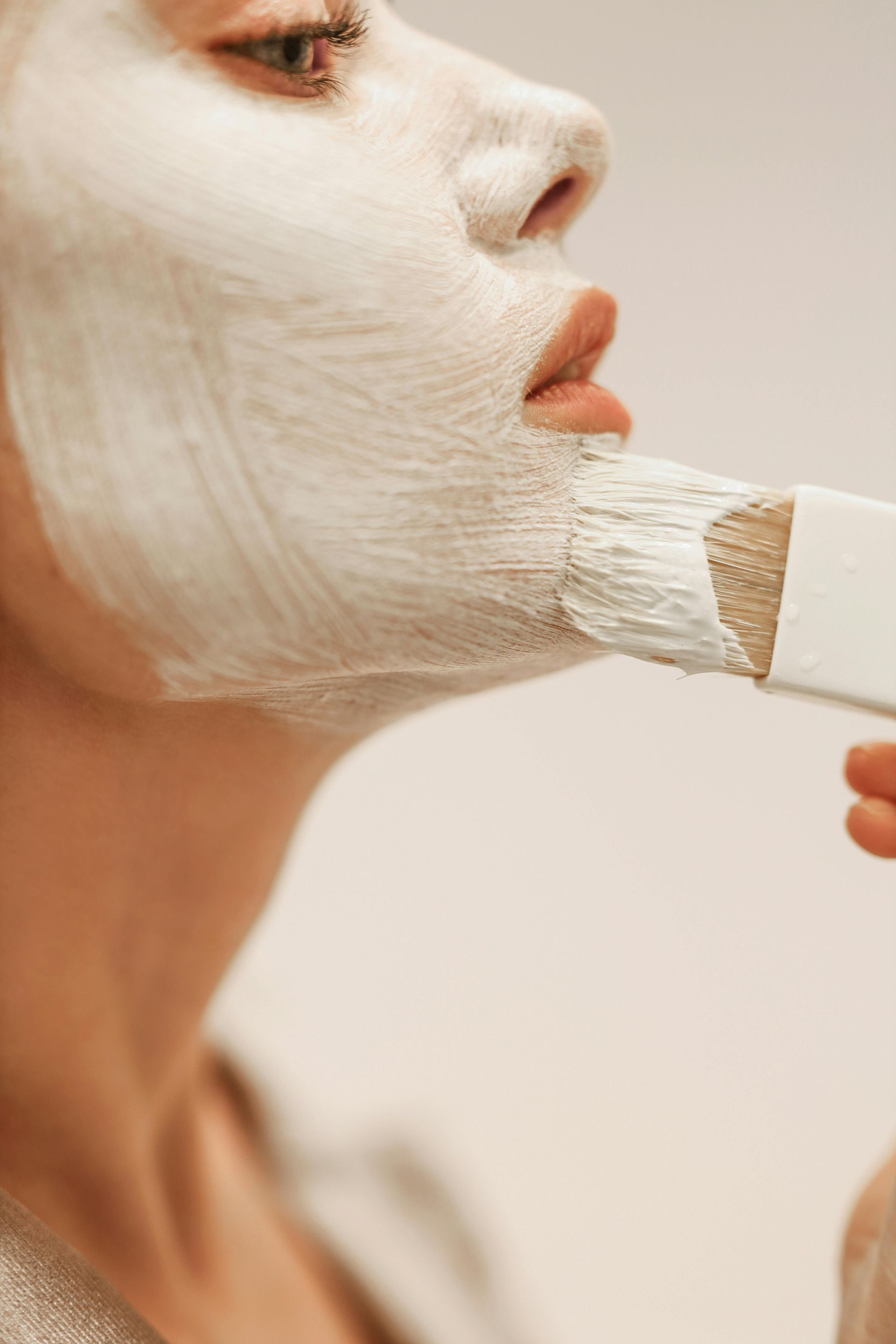 A woman is applying a white mask to her face with a brush.