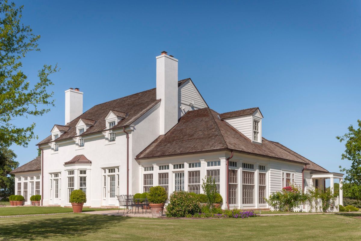 a large white house with a brown roof is sitting on top of a lush green field .