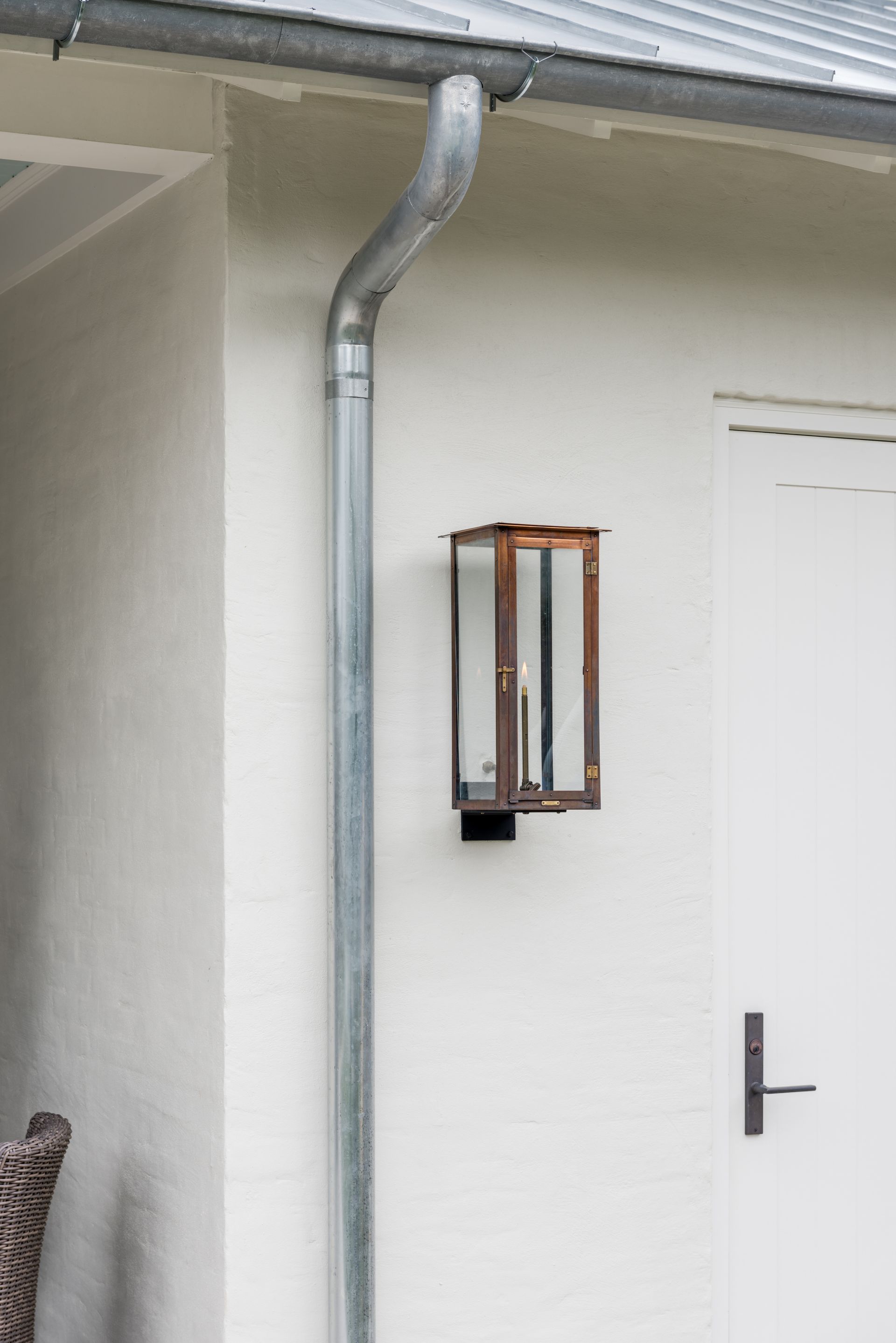 a white wall with a gutter and a lantern on it