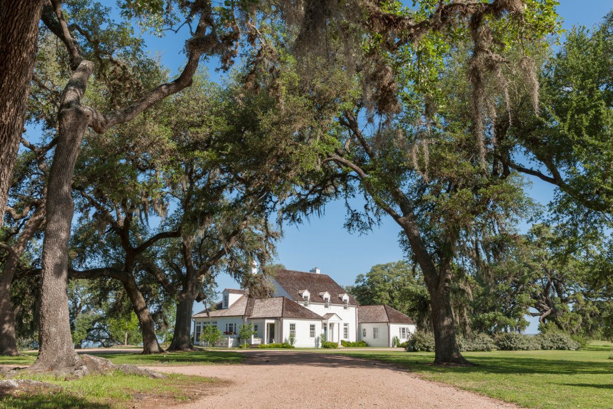 a large white house is surrounded by trees on a dirt road .