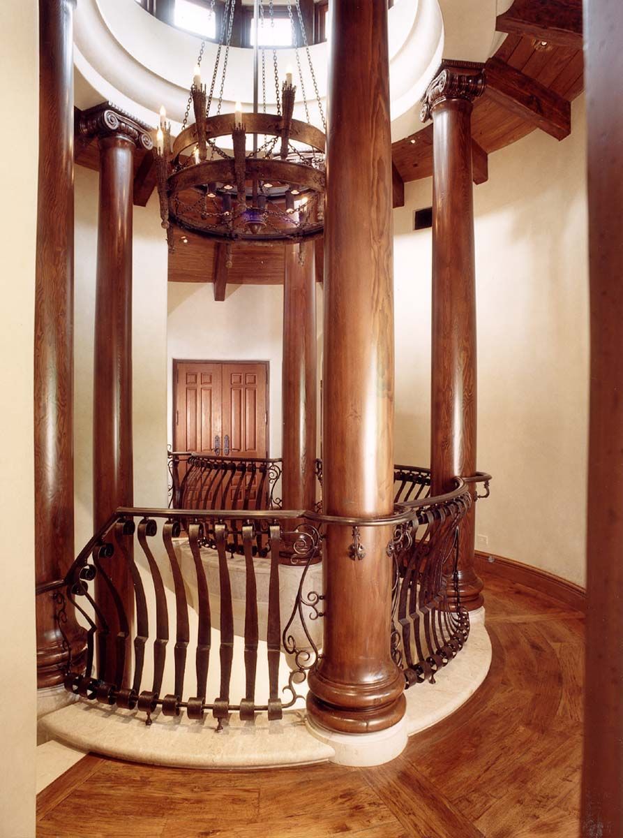 a spiral staircase with wooden columns and a chandelier hanging from the ceiling