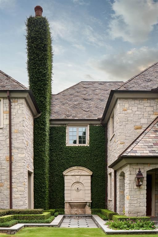 a large brick house with a chimney covered in greenery and a fountain in front of it .