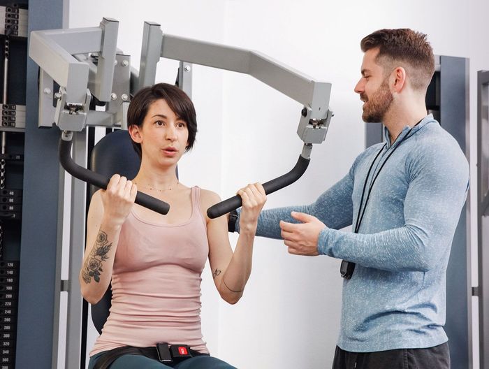 A Man Is Helping A Woman Exercise On A Machine In A Gym - Palm Desert, CA - The Strength Code Palm Desert