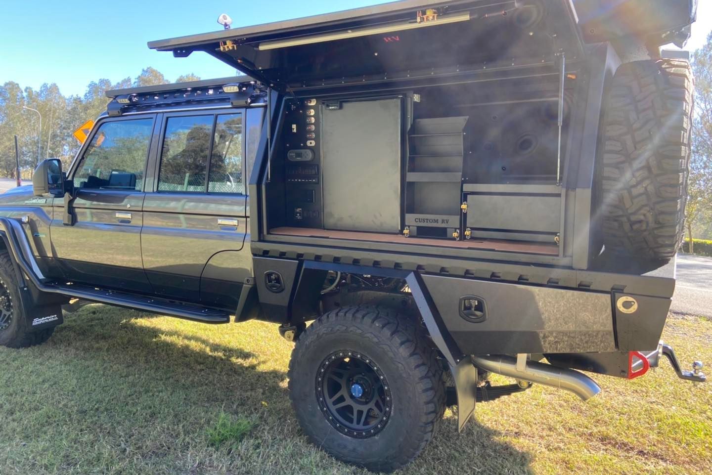 Black 4x4 truck with a customized utility bed. Open side shows shelving and storage. Outdoors. — Custom RV Creations & Repairs in Sumner, QLD