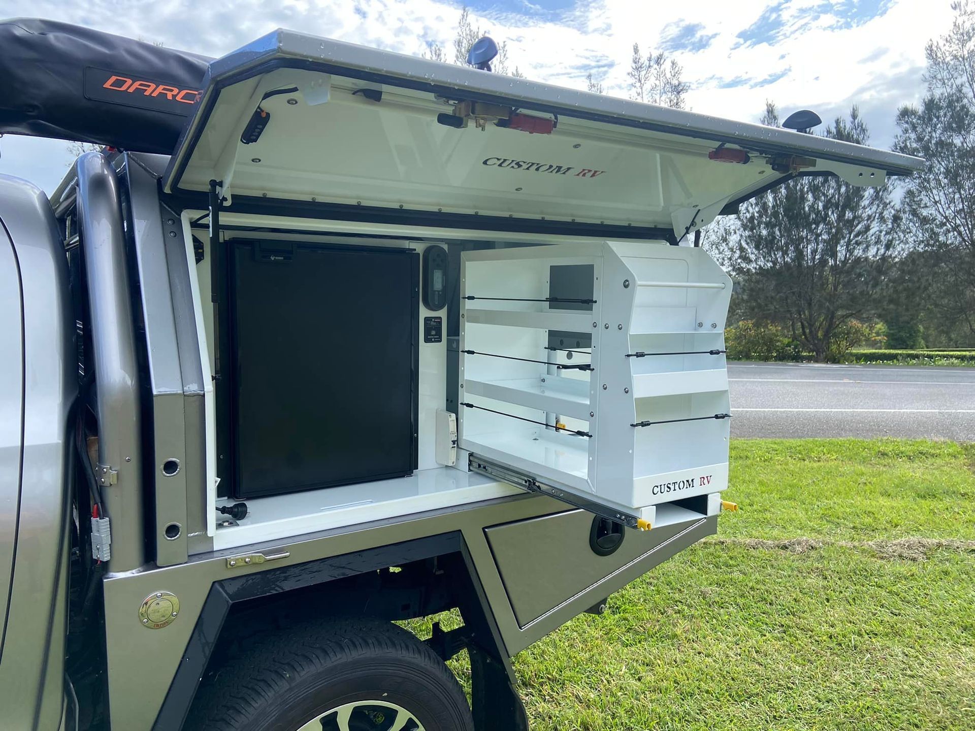 Silver truck bed with open storage compartment, showing refrigerator and shelves. Outdoors, daytime. — Custom RV Creations & Repairs in Sumner, QLD