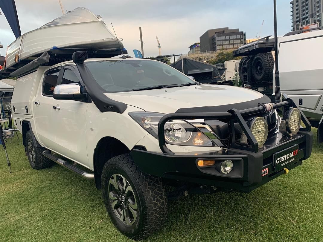 A White Vehicle With a Boat on Top of It is Parked in a Grassy Field — Custom RV Creations & Repairs in Gold Coast, QLD