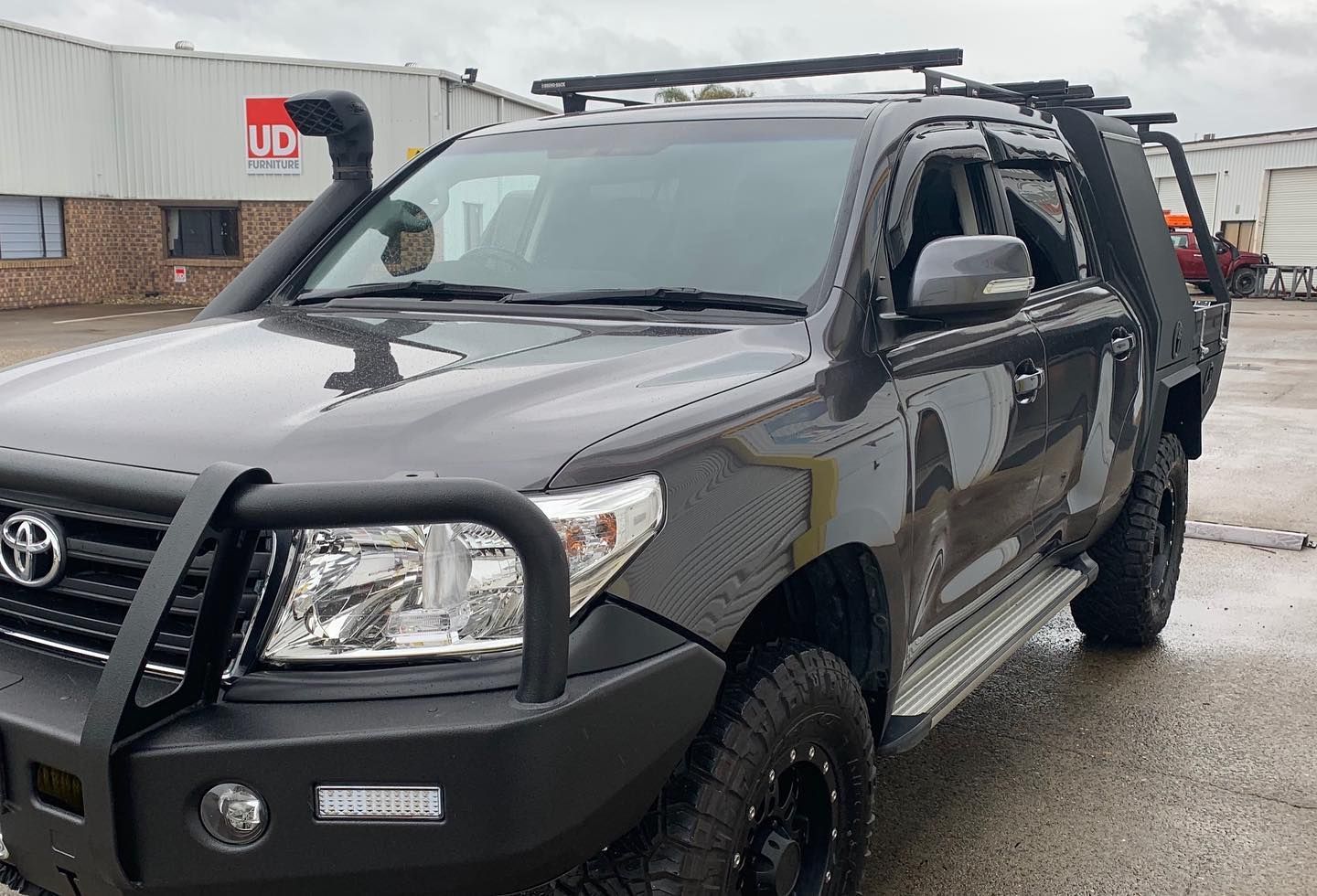 Dark gray Toyota Land Cruiser with off-road modifications: snorkel, bull bar, roof rack, and tray back. — Custom RV Creations & Repairs in Ipswich, QLD