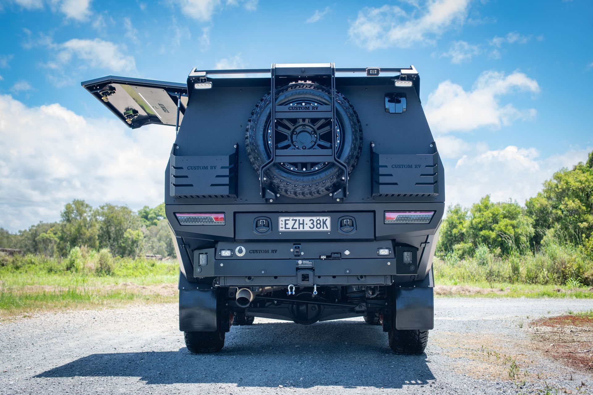 Black Off-road Vehicle With Spare Tire, Open Rear Door, and Trailer Hitch on a Gravel Road — Custom RV Creations in Sumner, QLD
