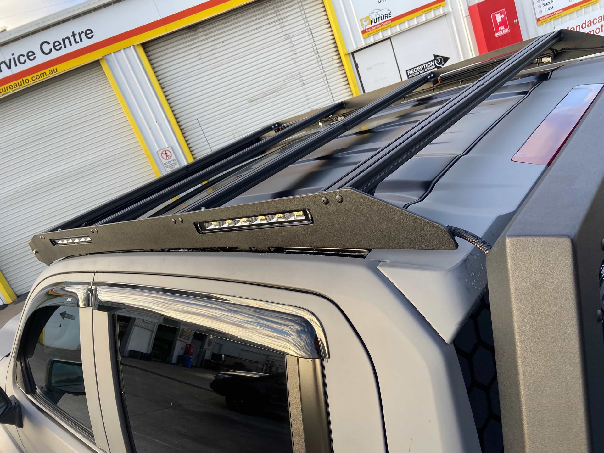 Black roof rack with LED light bar installed on a gray pickup truck, outside a service center. — Custom RV Creations & Repairs in Sumner, QLD