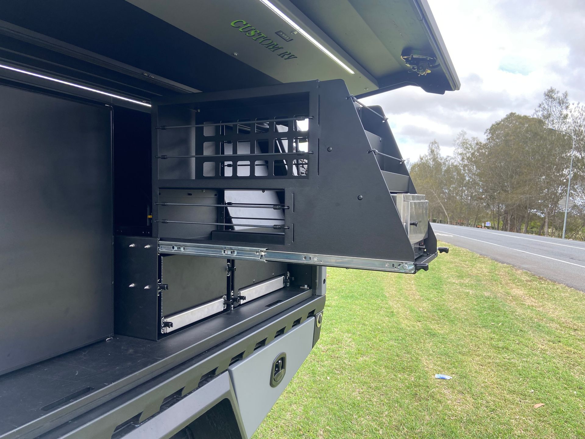Black Utility Box With Pull-out Drawers, Shelves, and Storage Compartments, Open Next to a Road, on Grass — Custom RV Creations in Sumner, QLD
