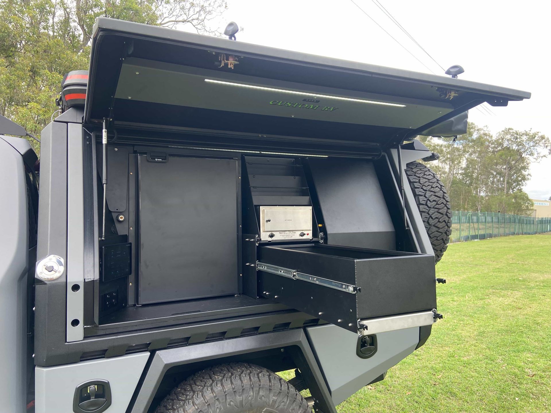 Gray truck bed with open canopy revealing a refrigerator, drawer, and storage compartments. — Custom RV Creations & Repairs in Sumner, QLD
