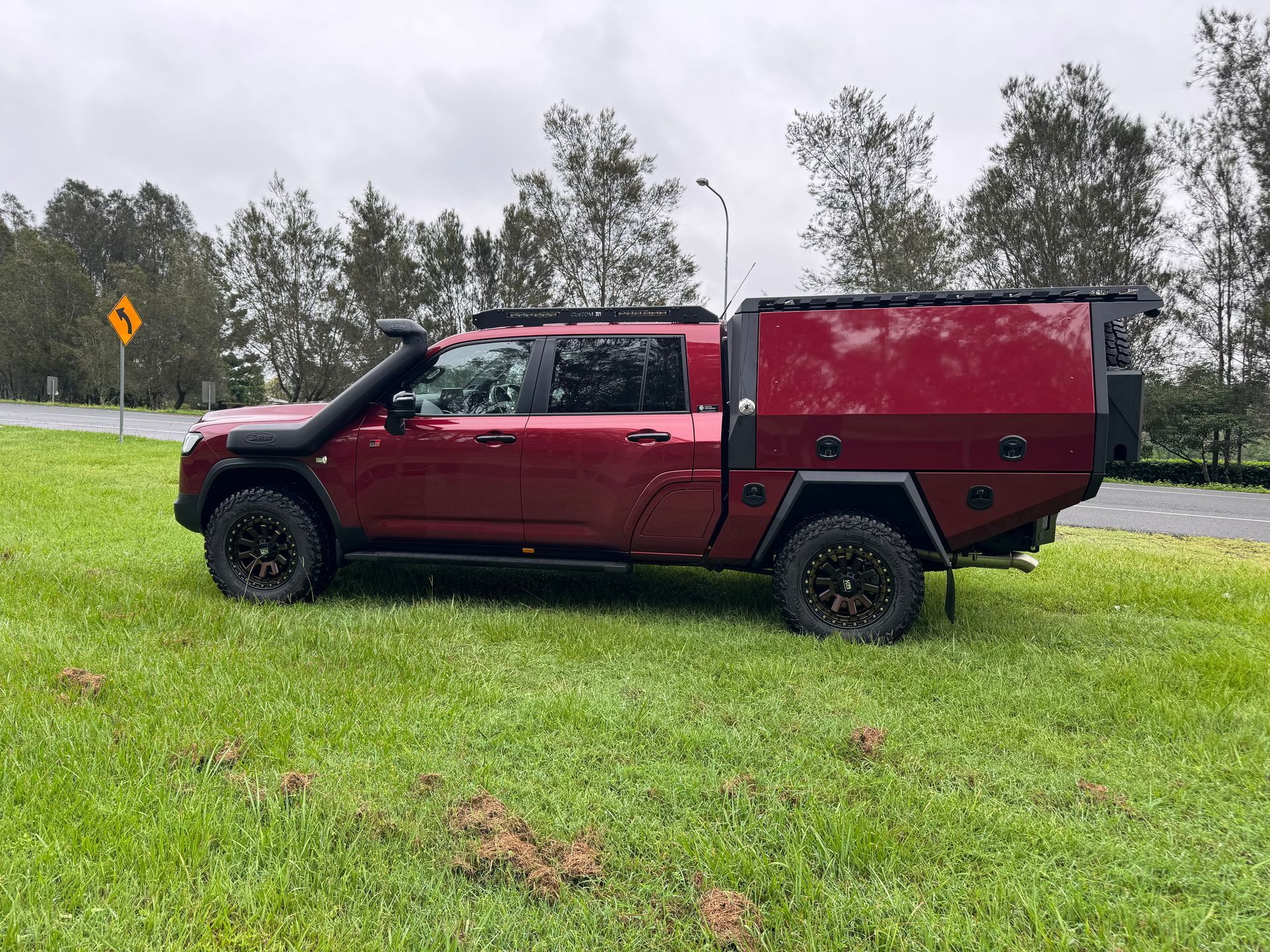 Red Pickup Truck With Black Off-road Wheels and Camper Top Parked on Grass — Custom RV Creations in Sumner, QLD