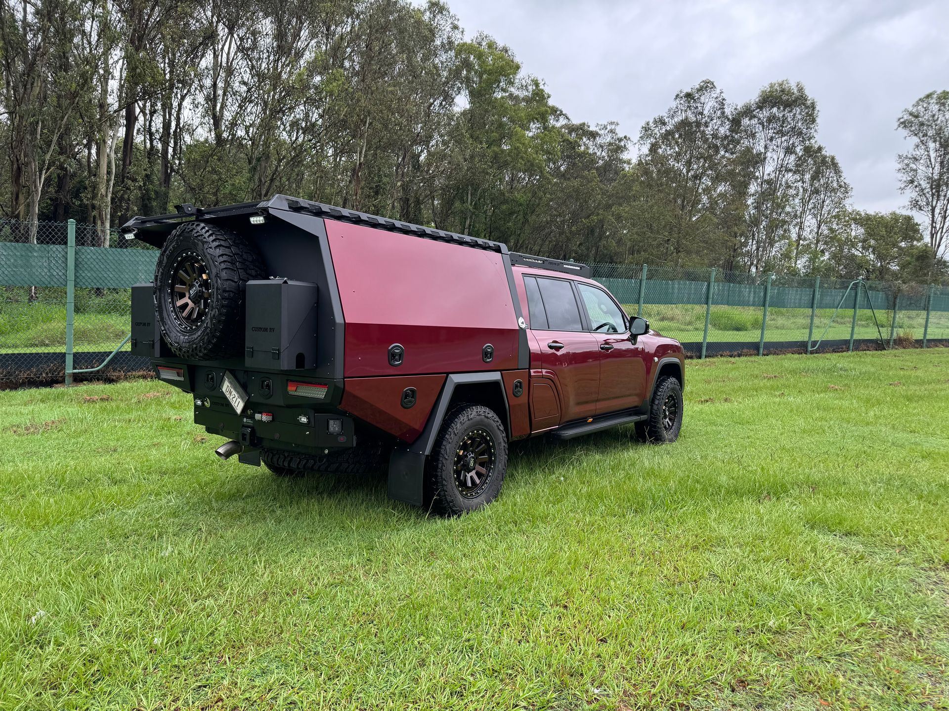 Burgundy Truck With Camper Shell Parked on Grass Near a Fence — Custom RV Creations in Sumner, QLD