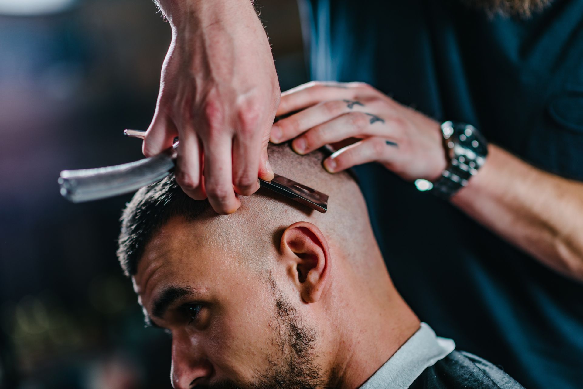 A barber using a straight razor to shave a customer's head in a professional setting.