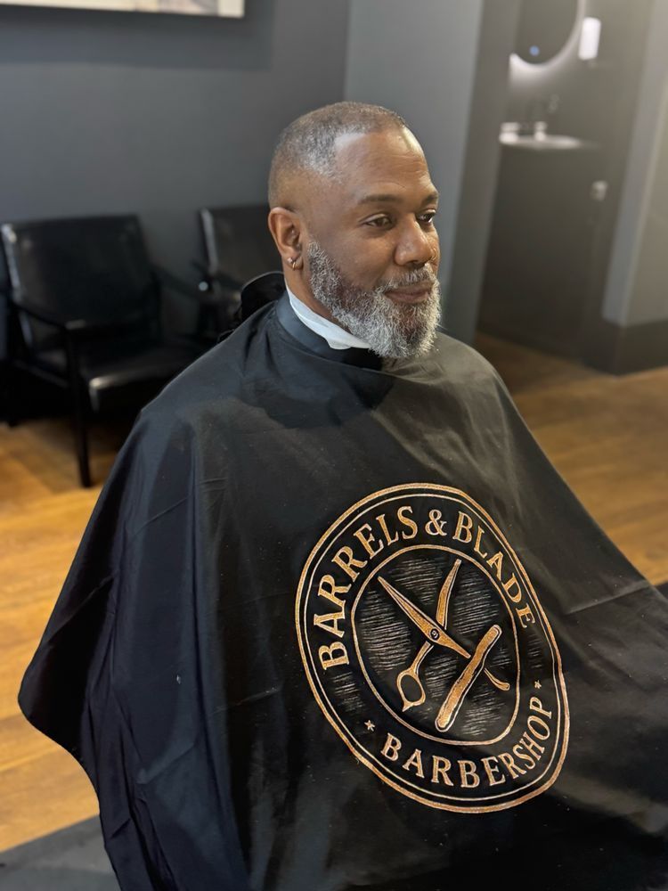 Man sitting in a barber chair wearing a black cape in a barbershop.