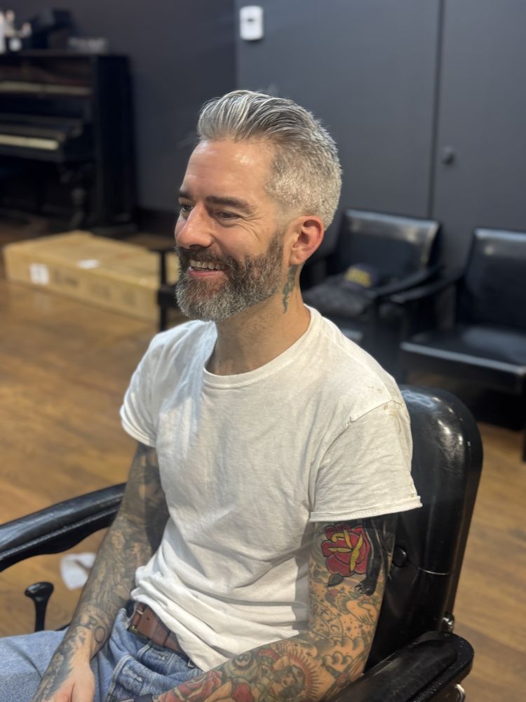 Smiling man with tattoos seated in a black chair in a studio with boxes and chairs in the background