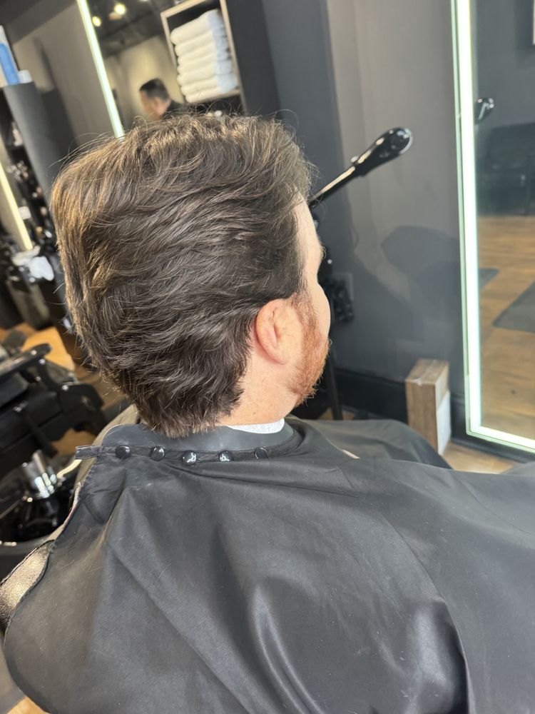 Person with medium brown hair and layered cut seated in a salon chair, seen from behind.