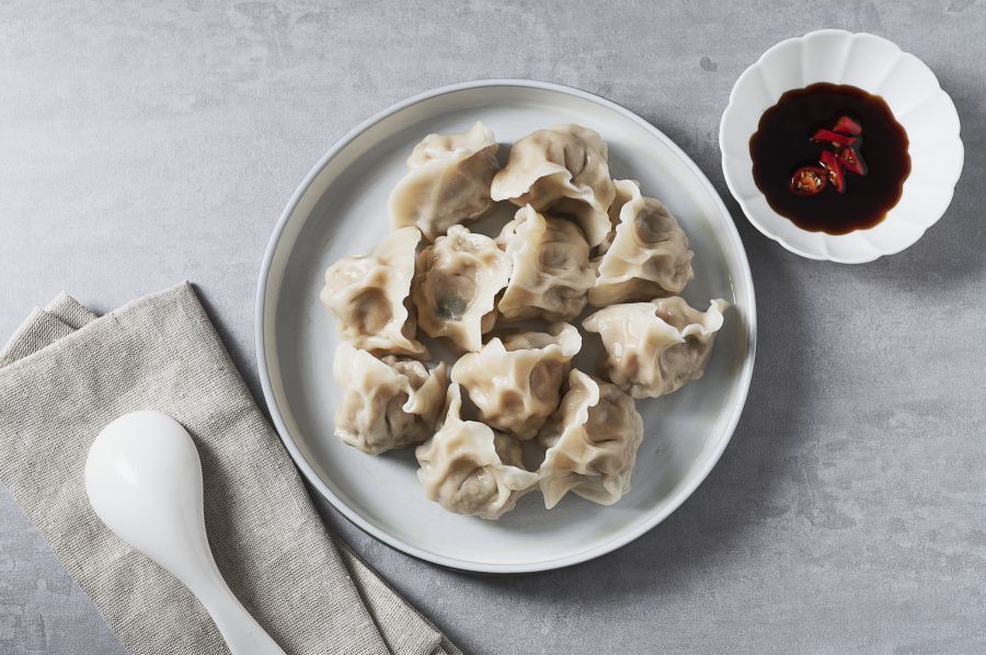 Dumplings on plate, held by chopsticks, with soy sauce and spoon on a table.