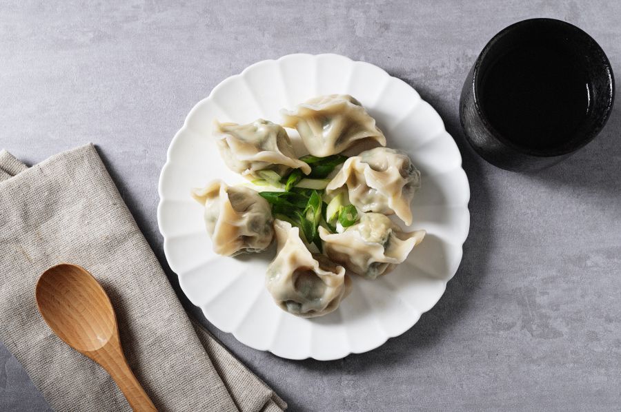 Plate of dumplings with chopsticks holding one, soy sauce, and a spoon.