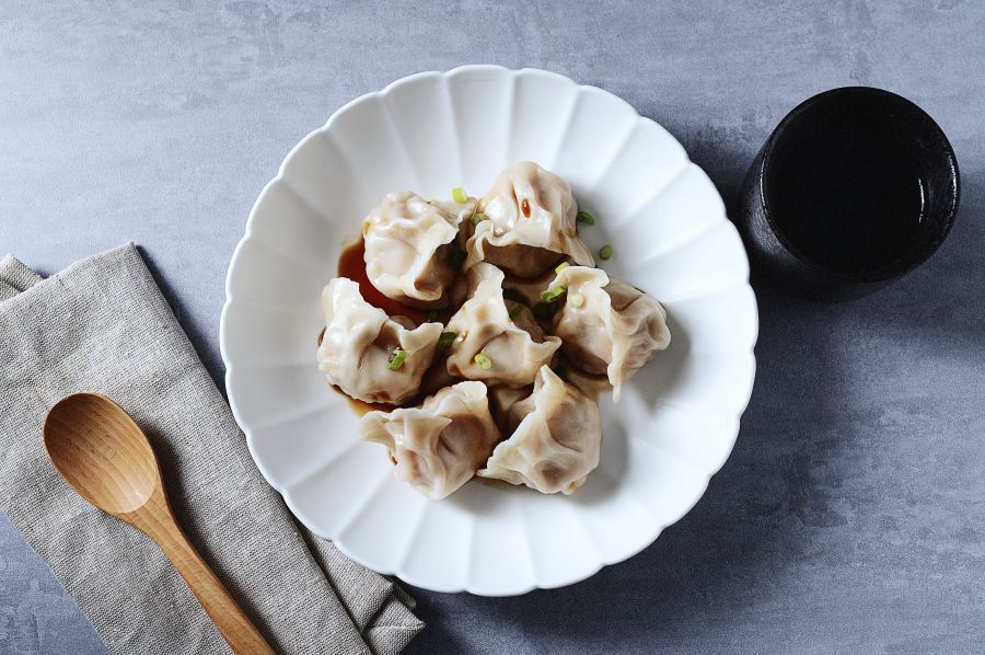Dim sum held in chopsticks, with a plate of dim sum and dipping sauce in the background.