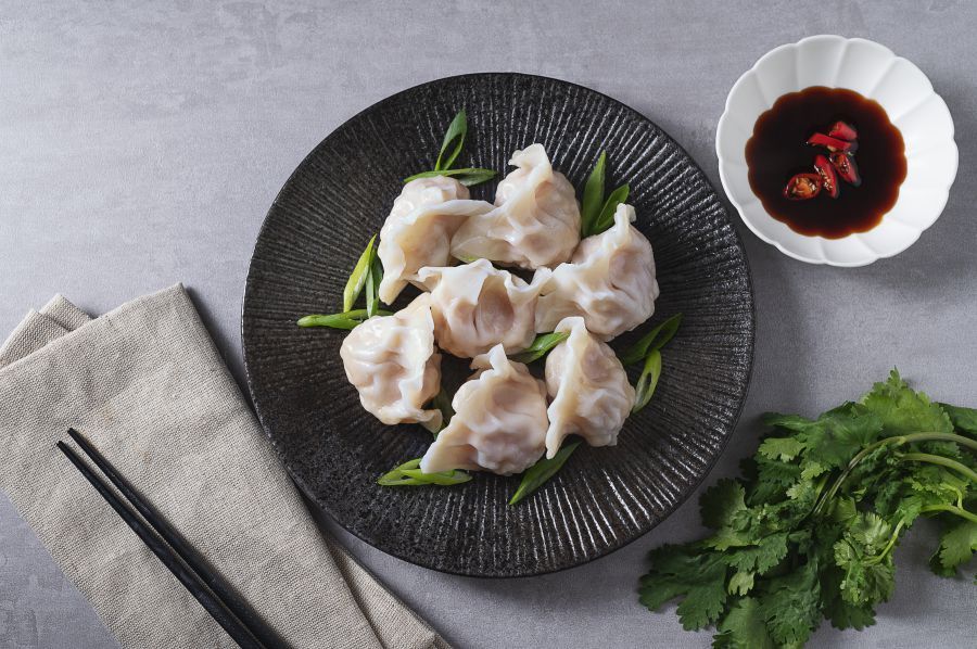 Dumpling held by chopsticks, revealing corn and filling. Plate with more dumplings and soy sauce.